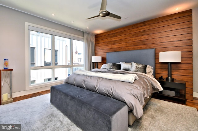 bedroom featuring ceiling fan, wood-type flooring, wooden walls, and multiple windows