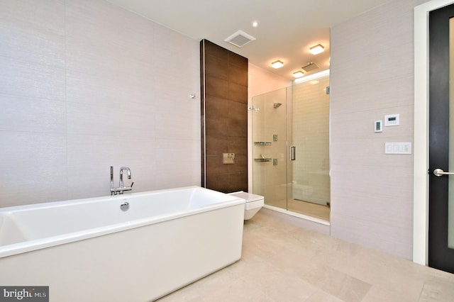 bathroom featuring tile patterned floors, toilet, tile walls, and plus walk in shower