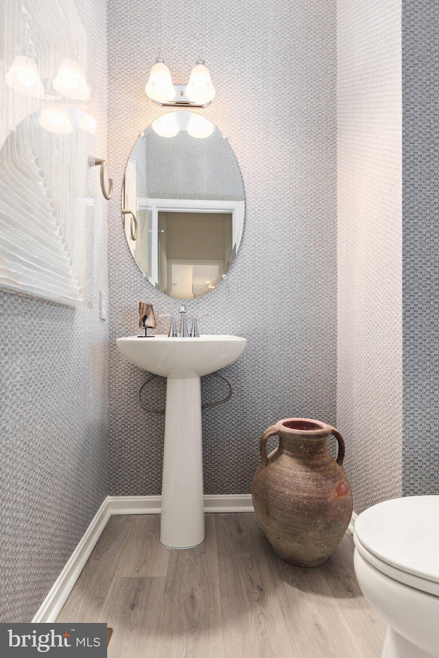 half bath featuring a sink, toilet, baseboards, and wood finished floors