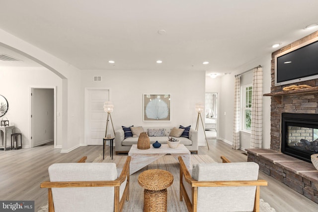 living room with light wood finished floors, visible vents, baseboards, a fireplace, and arched walkways