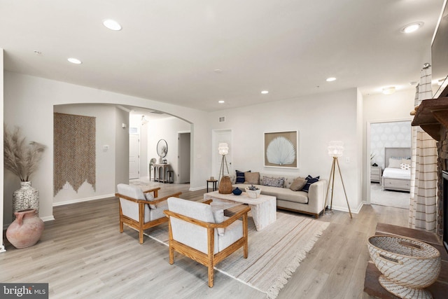 living room featuring baseboards, light wood-style flooring, a fireplace, recessed lighting, and arched walkways