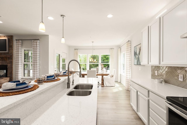 kitchen with tasteful backsplash, light stone countertops, light wood-type flooring, hanging light fixtures, and a sink