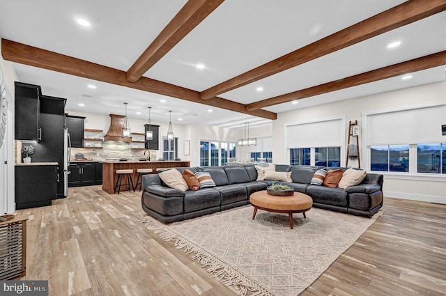 living room with an inviting chandelier, sink, beam ceiling, and light hardwood / wood-style flooring