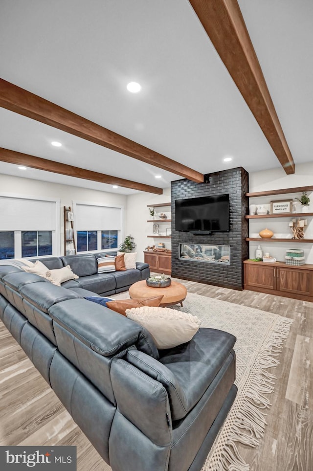 living room with beamed ceiling, light wood-type flooring, and a brick fireplace