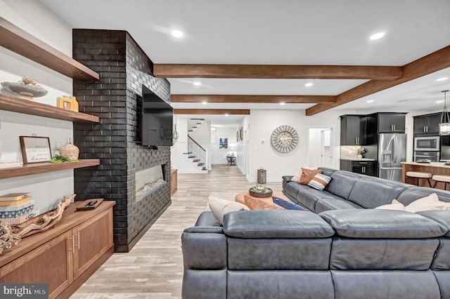 living room featuring light hardwood / wood-style flooring, beamed ceiling, and a brick fireplace