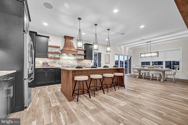 kitchen featuring a kitchen breakfast bar, light wood-type flooring, a center island with sink, and hanging light fixtures