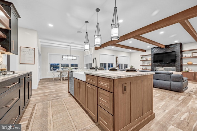 kitchen with light stone countertops, light wood-type flooring, decorative light fixtures, and a kitchen island with sink