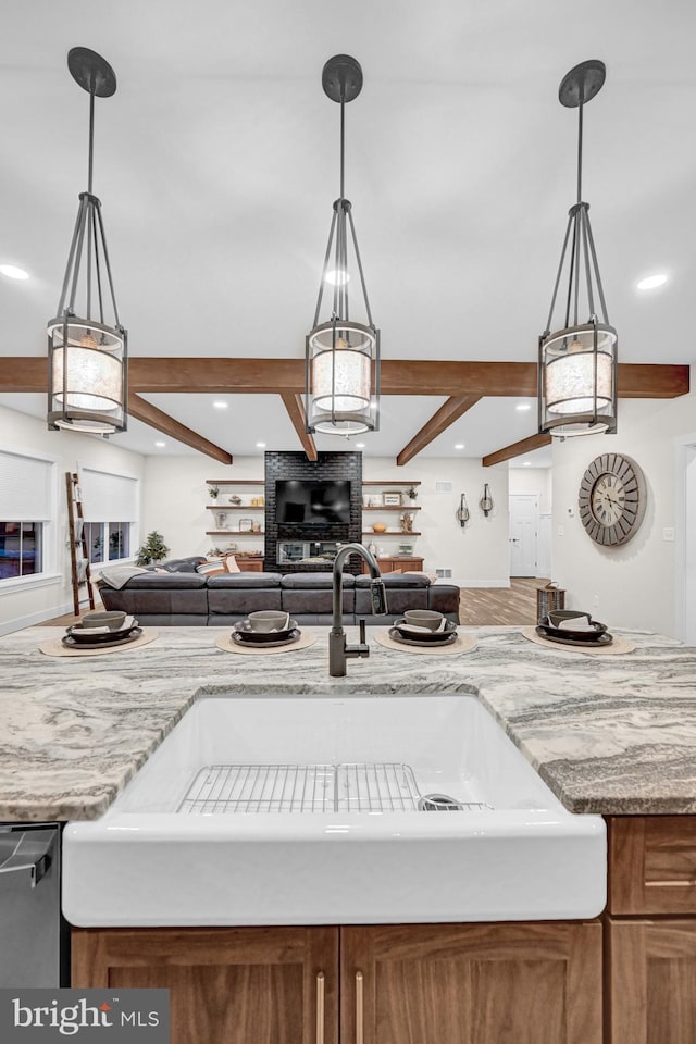 kitchen with beamed ceiling, pendant lighting, light stone countertops, and sink