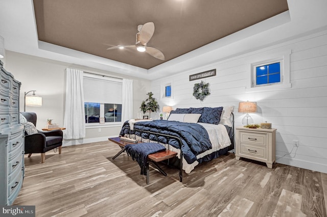 bedroom with a raised ceiling, ceiling fan, and light hardwood / wood-style floors