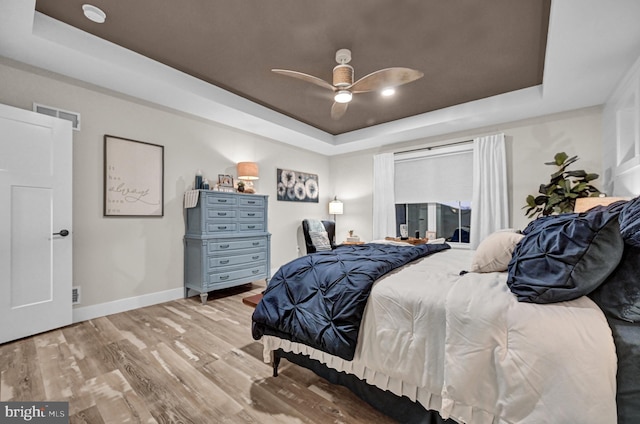 bedroom featuring light hardwood / wood-style flooring, a raised ceiling, and ceiling fan