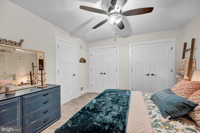 carpeted bedroom featuring multiple closets and ceiling fan