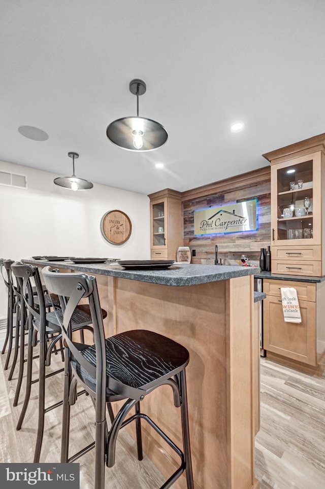 bar with decorative light fixtures, wooden walls, and light hardwood / wood-style flooring