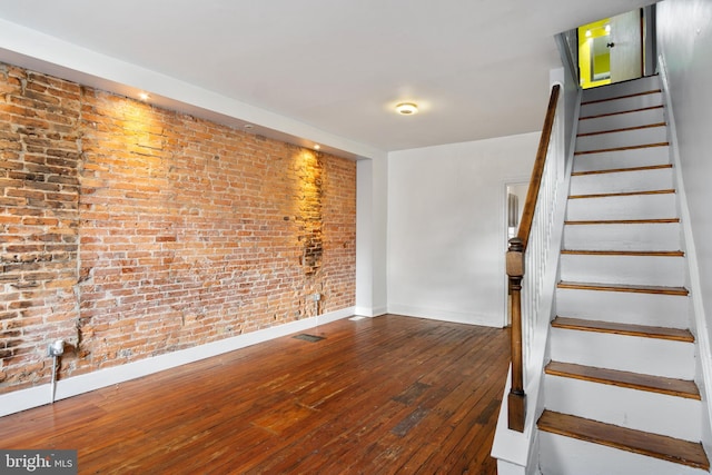 staircase with wood-type flooring and brick wall