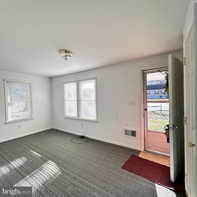 entrance foyer with plenty of natural light and dark colored carpet