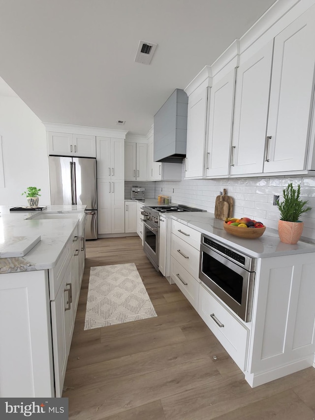 kitchen featuring backsplash, premium range hood, stainless steel appliances, light hardwood / wood-style floors, and white cabinetry