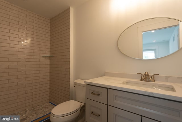 bathroom featuring a tile shower, vanity, and toilet