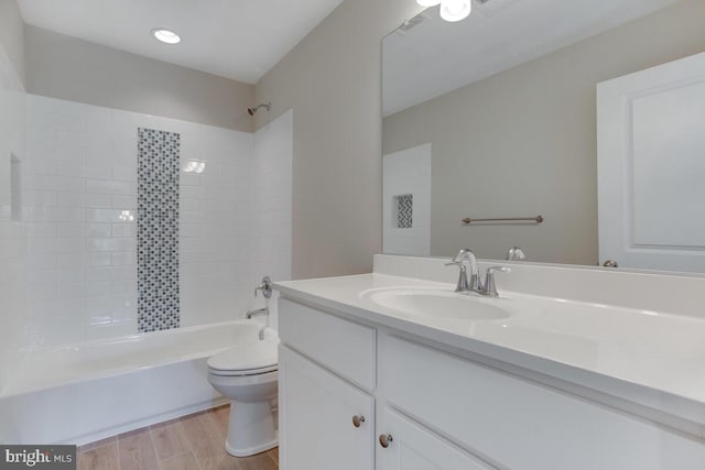 full bathroom with hardwood / wood-style floors, vanity, tiled shower / bath combo, and toilet