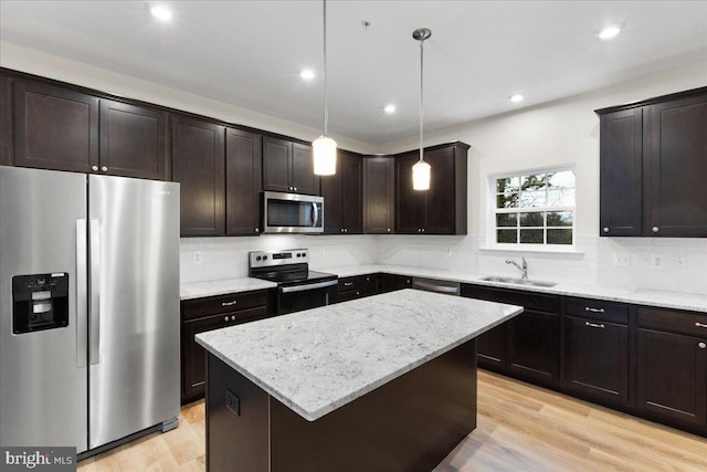 kitchen with appliances with stainless steel finishes, sink, decorative light fixtures, light hardwood / wood-style flooring, and a kitchen island