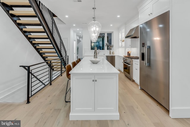 kitchen featuring pendant lighting, high quality appliances, wall chimney exhaust hood, a kitchen island, and white cabinetry