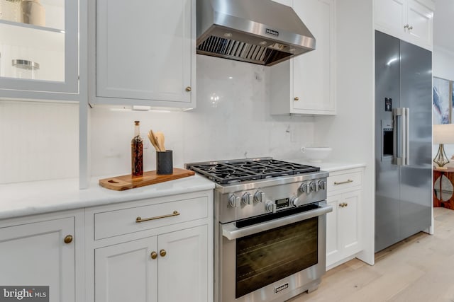 kitchen featuring light wood-type flooring, tasteful backsplash, wall chimney exhaust hood, high quality appliances, and white cabinetry