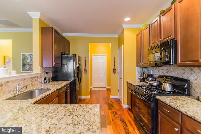 kitchen with sink, crown molding, dark wood-type flooring, light stone counters, and black appliances