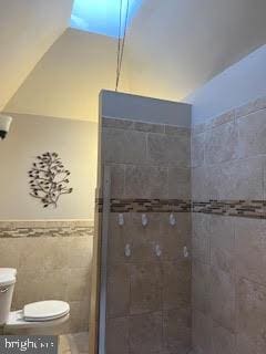 bathroom with a tile shower, toilet, and tile walls