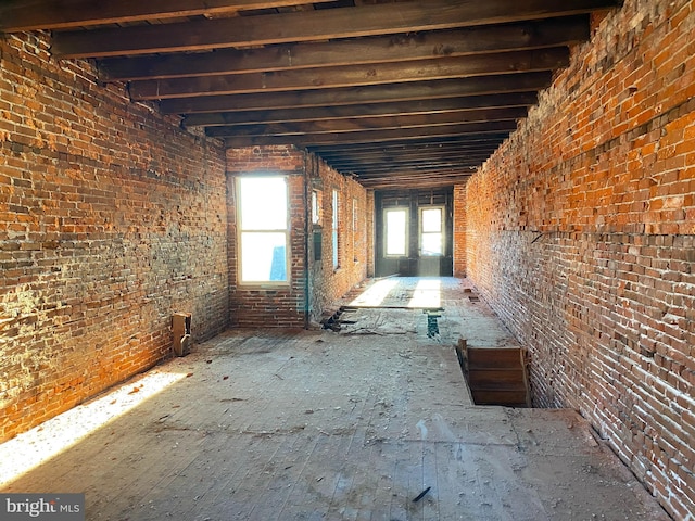 misc room featuring beamed ceiling and brick wall