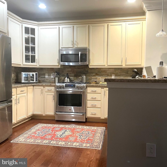 kitchen with pendant lighting, dark stone counters, dark hardwood / wood-style floors, tasteful backsplash, and stainless steel appliances