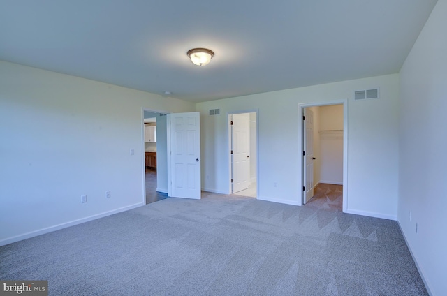 unfurnished bedroom featuring a spacious closet, carpet, visible vents, and baseboards