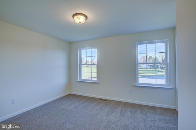 spare room featuring dark colored carpet, visible vents, and baseboards