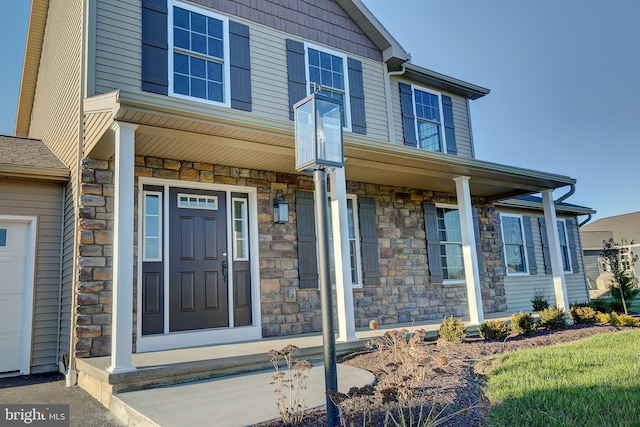 entrance to property with a garage, stone siding, and a porch