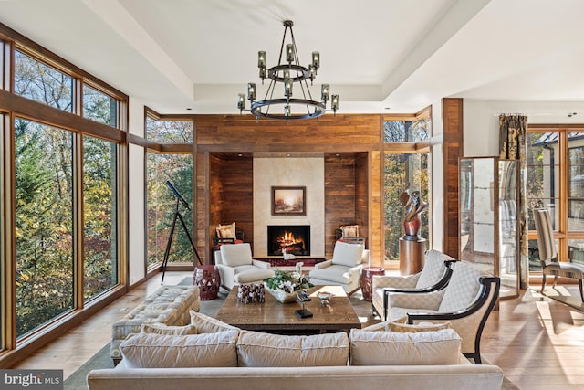 living room featuring a raised ceiling, light hardwood / wood-style flooring, built in features, a large fireplace, and a notable chandelier