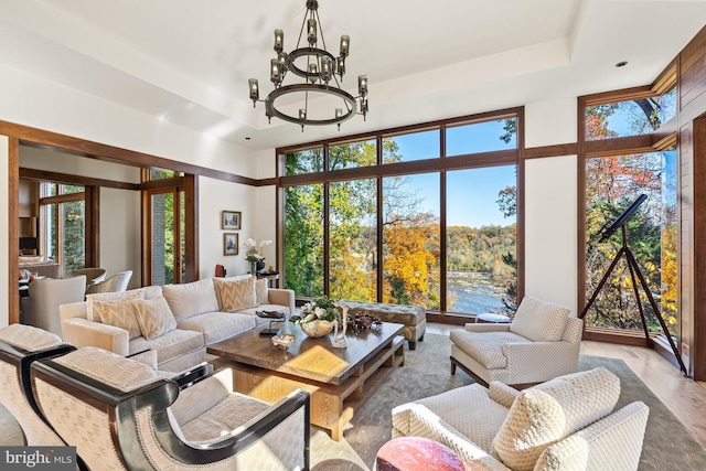 living room with a chandelier, a wall of windows, a raised ceiling, and light hardwood / wood-style floors