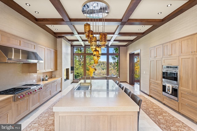 kitchen with coffered ceiling, a center island with sink, light tile floors, wall chimney range hood, and beam ceiling