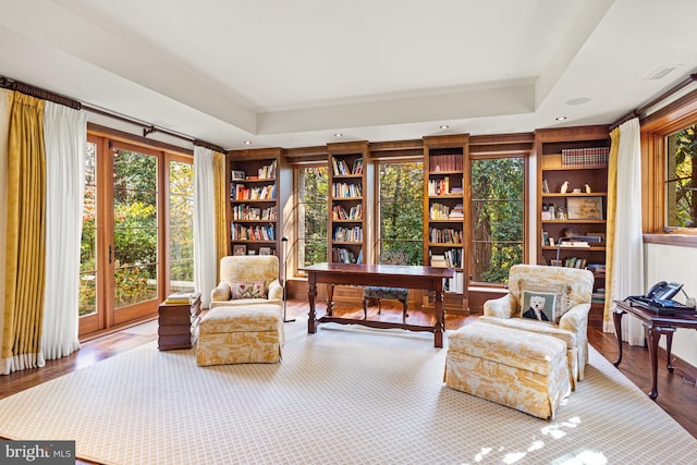 living area featuring built in features, light wood-type flooring, and a tray ceiling