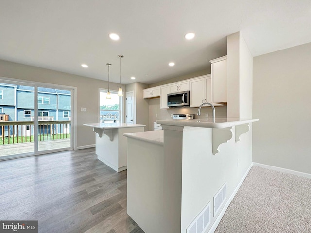 kitchen with white cabinets, kitchen peninsula, hanging light fixtures, light wood-type flooring, and a kitchen breakfast bar