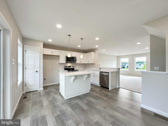 kitchen with white cabinetry, a center island, carpet floors, stainless steel appliances, and decorative light fixtures