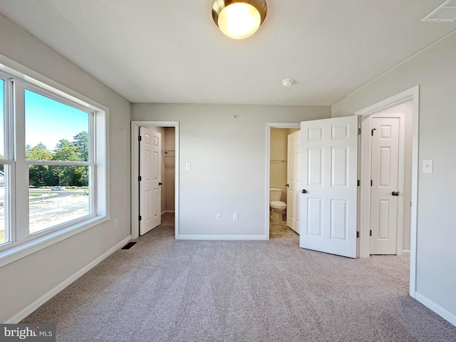 unfurnished bedroom featuring carpet floors, ensuite bathroom, a spacious closet, and a closet