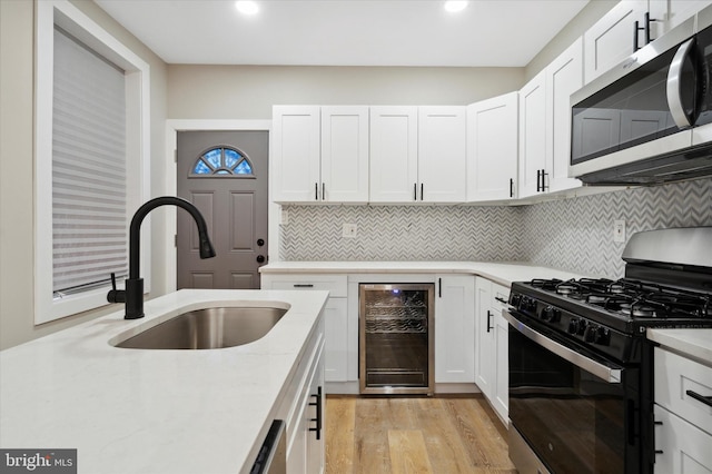 kitchen featuring gas stove, sink, white cabinets, light hardwood / wood-style floors, and beverage cooler