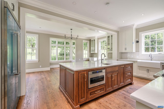 kitchen with appliances with stainless steel finishes, white cabinets, sink, light wood-type flooring, and a center island with sink