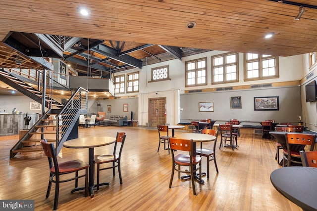 dining area with wooden ceiling, a wealth of natural light, light wood-type flooring, and a towering ceiling