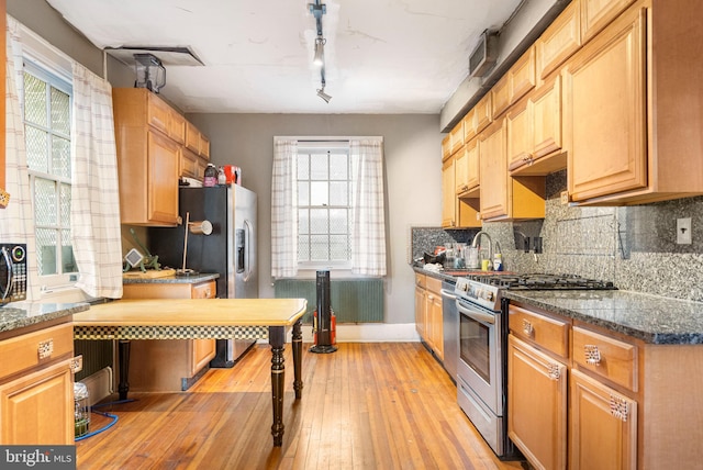 kitchen featuring dark stone counters, stainless steel gas range, light hardwood / wood-style flooring, and a wealth of natural light