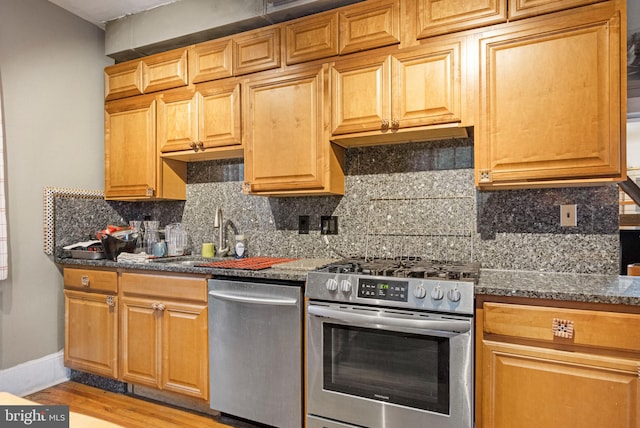 kitchen with sink, light hardwood / wood-style flooring, stainless steel appliances, dark stone counters, and tasteful backsplash