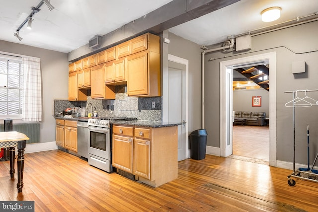 kitchen featuring light hardwood / wood-style floors, sink, stainless steel appliances, dark stone counters, and tasteful backsplash