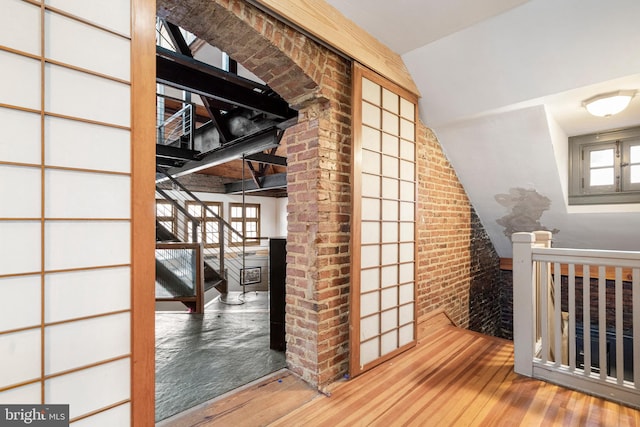 interior space featuring lofted ceiling, light hardwood / wood-style flooring, and brick wall