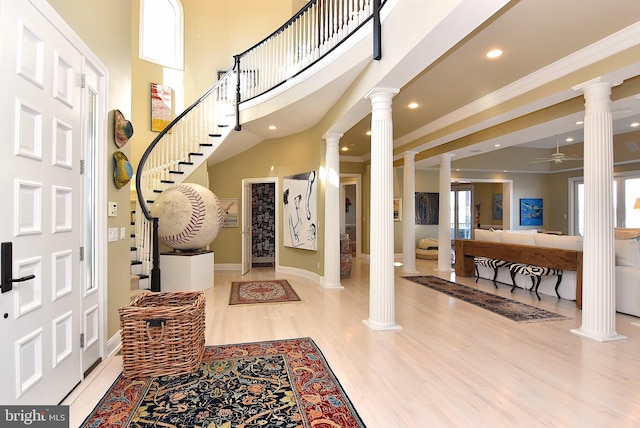 foyer featuring a high ceiling, ceiling fan, ornamental molding, light hardwood / wood-style flooring, and ornate columns