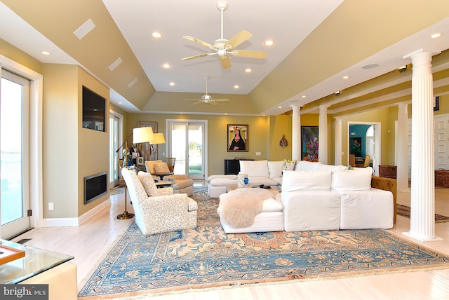 living room with light hardwood / wood-style floors, decorative columns, ceiling fan, and a tray ceiling