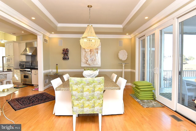 dining area featuring a raised ceiling, ornamental molding, a notable chandelier, and light wood-type flooring