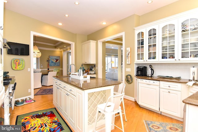 kitchen with dark stone counters, tasteful backsplash, white cabinets, light wood-type flooring, and sink