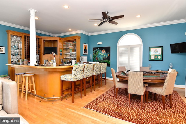 kitchen with a kitchen breakfast bar, ornamental molding, decorative columns, and light wood-type flooring